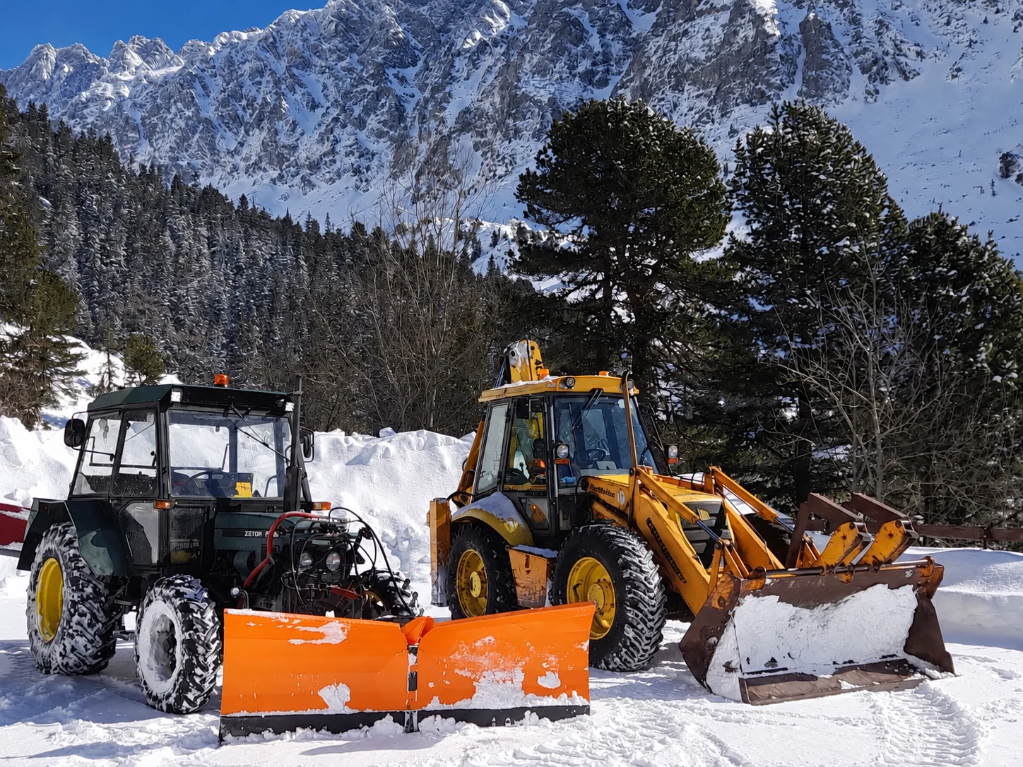 Traktor a traktorbager pod zasneženými Tatrami